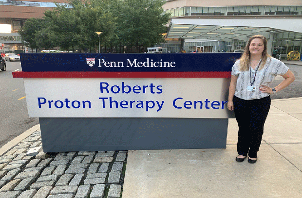 Patient Engagement Intern Peri Niskey standing by the Roberts Proton Therapy Center sign