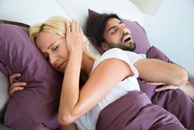  Young woman is very irritated by her boyfriends snoring and covering her ears with her hands