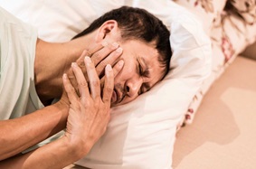 TMJ Pain Male Holding Face In Bed
