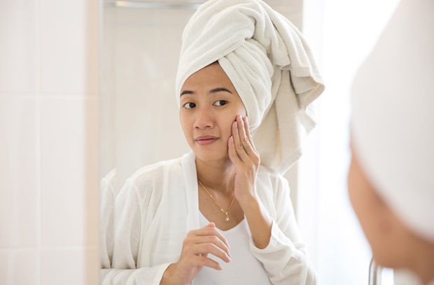 Woman wearing towel examining face in mirror