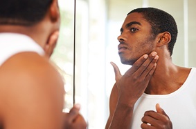 young_man_looks_at_face_along_jawline_in_mirror_checking_skin