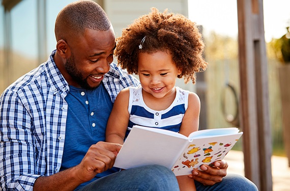 Dad and daughter laughing while reading a children's book