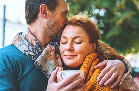 middle aged men and women share a hug together as man holds coffee cup outside