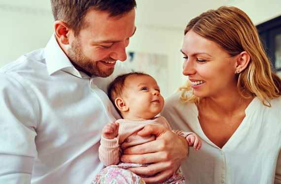 Young mom and dad smiling while holding newborn daughter