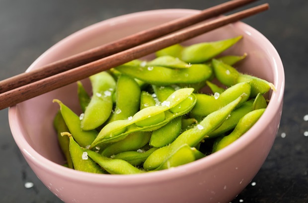 Edamame pods in a pink bowl with chopsticks