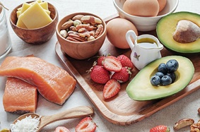 cheese_in_bowl_nuts_in_bowl_eggs_sliced_avocado_blueberries_strawberries_salmon_coconut_healthy_fats_for_keto_diet