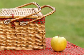 a picnic basket next to an apple on a table cloth