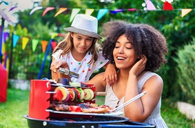 A woman and a young girl grilling vegetables at a backyard barbecue