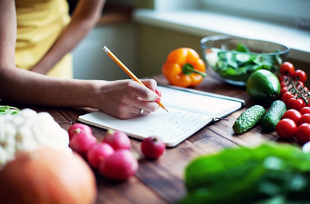 Woman writing in food journal surrounded by vegetables