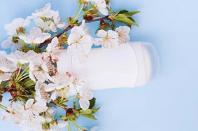 white_stick_of_deodorantlays_on_pale_blue_background_with_small_light_pink_flowers