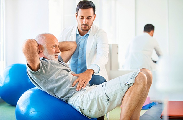physical therapist guiding a man doing situps on a balance ball