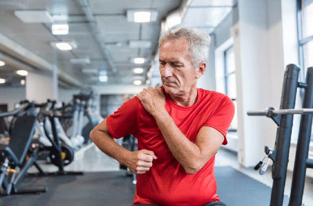 Man sitting in the gym and holding shoulder in pain