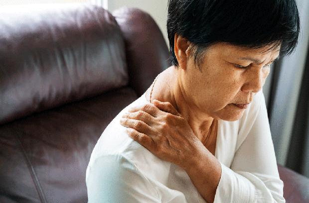 older woman sitting down and holding shoulder in pain