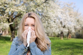 woman blowing her nose with blossoming trees in the background