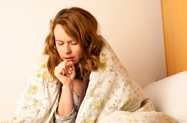 sick woman sitting in bed and coughing