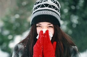 woman in winter clothes sneezing