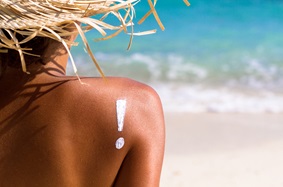 woman tanning on the beach with an exclamation point drawn on her back with sunscreen