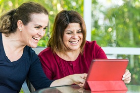 Two middle-aged women smiling surfing the net