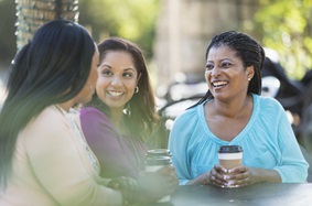 3 women talking over coffee at an outside table