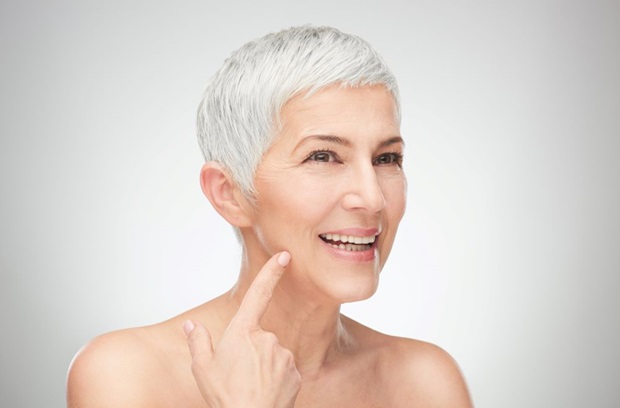 Older Woman Pointing to Jawline Smiling