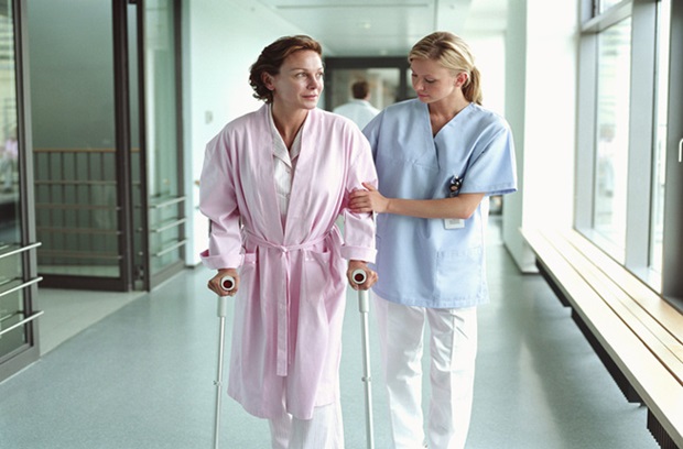 Nurse helping patient walk down hospital corridor