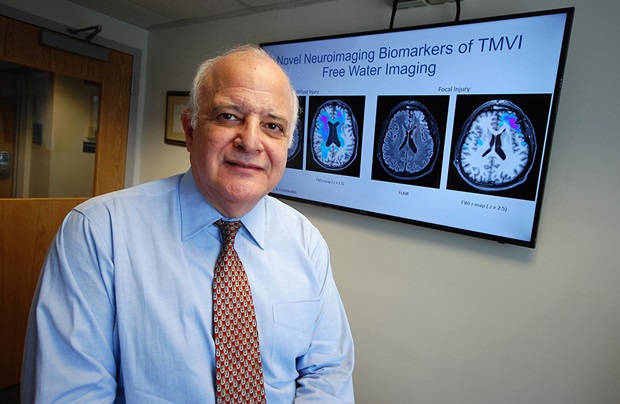 Dr. Diaz-Arrastia in front of a sign about Traumatic Brain Injuries