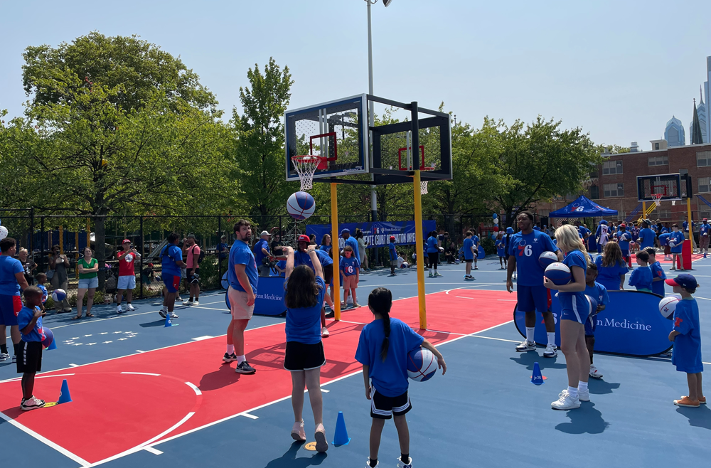 Families gather, in Philadelphia Sixers t-shirts, on the new basketball court in Roberto Clemente Park.